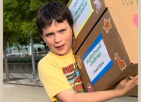 Boy in a yellow shirt carries two large boxes labeled “10,000 Pound Challenge Food Drive,” decorated with stickers.