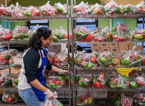 A volunteer organizes bags of fresh produce on metal shelves in a food pantry.